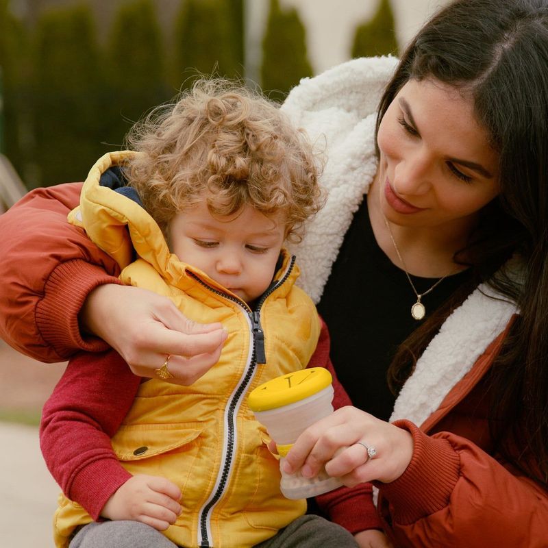 Toddler in a yellow jacket eating from the babygami snack cup outside